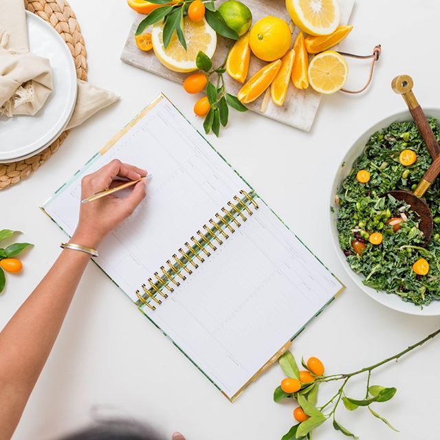A person writing in a wellness journal with fresh fruit on the table beside them